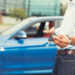 40416365 - male hand holding car keys offering new blue car on background