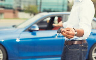 40416365 - male hand holding car keys offering new blue car on background